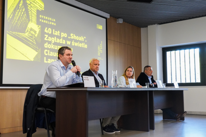 Cztery osoby, trzech mężczyzn i kobieta siedzą przy stole, w tle na ekranie grafika: dyskusja panelowa, 40 lat po Shoah Zagłada w świetle dokumentu (reszta nieczytelna) 