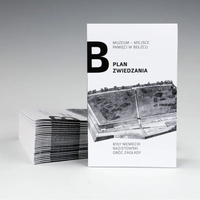Zdjęcie przedstawia pionowo ustawiony plan zwiedzania Muzeum – Miejsca Pamięci w Bełżcu na jasnym tle. Obok leży stos kolejnych, złożonych egzemplarzy. Okładka jest biała, zawiera dużą czarną literę „B”, napis „PLAN ZWIEDZANIA” oraz grafikę przedstawiającą widok z lotu ptaka na teren byłego niemieckiego nazistowskiego obozu zagłady. Design jest nowoczesny i minimalistyczny.