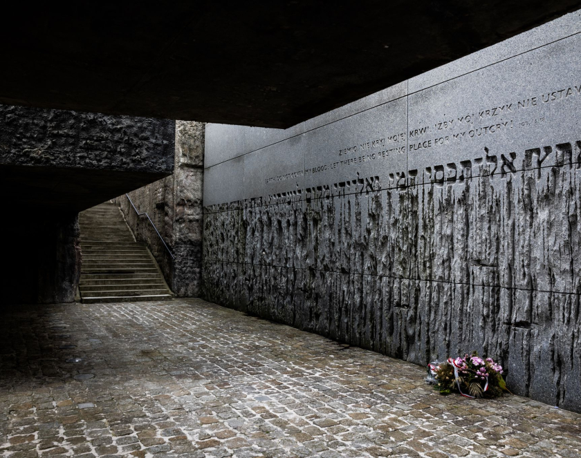 Fragment betonowego pomnika z wyrytą inskrypcją, wiązanka z kwiatów.