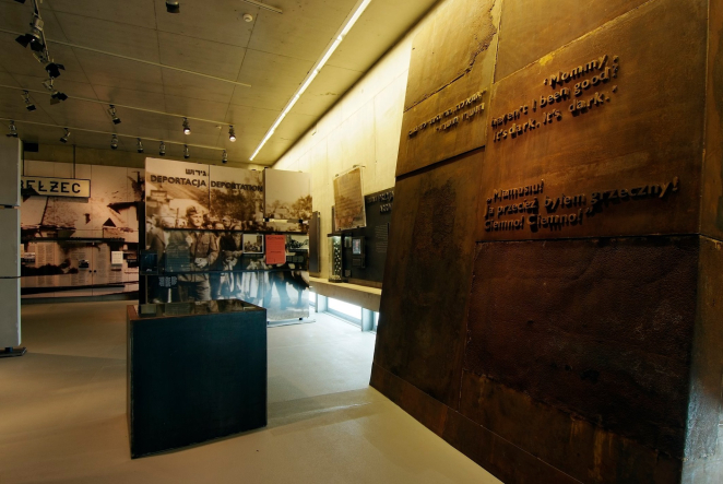 Wnętrze wstawy, metalowa plansza z inskrypcją, gablota wystawiennicza oraz zdjęcia historyczne. 