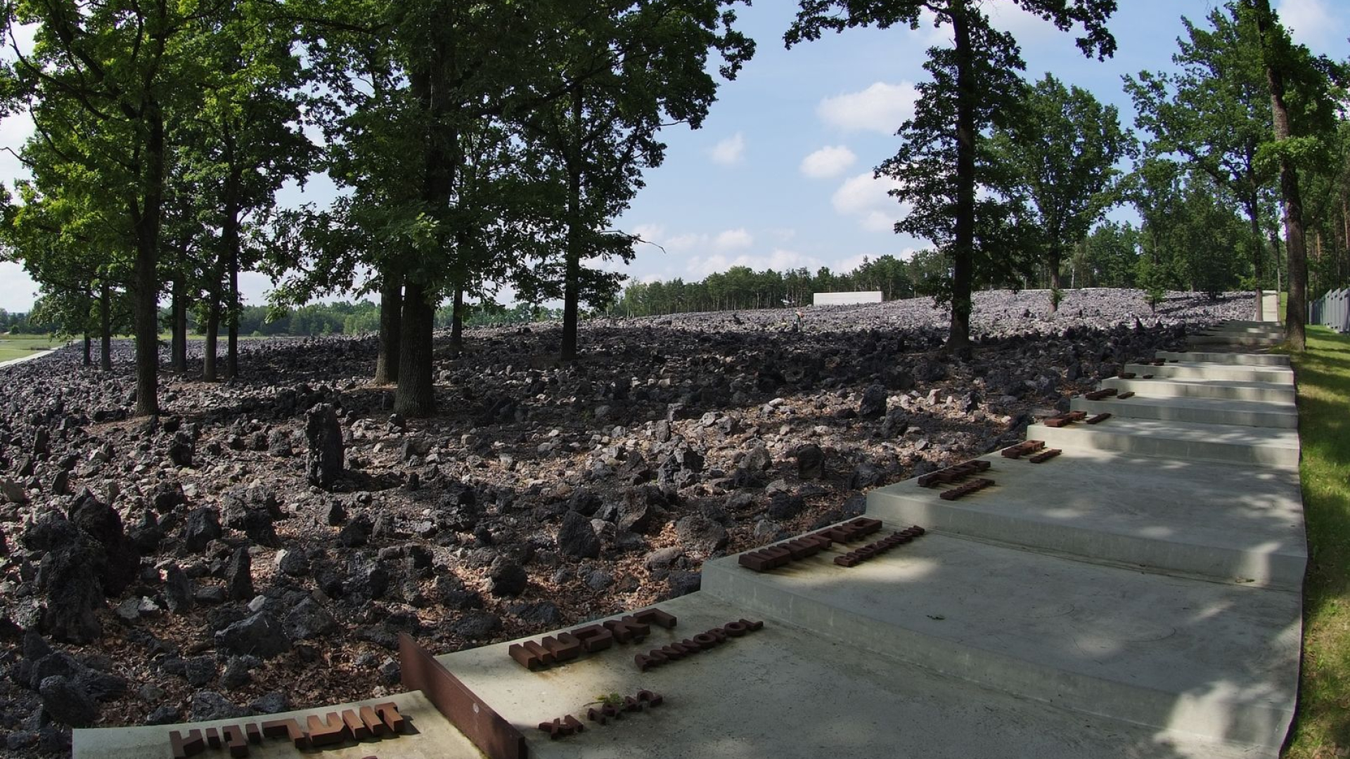 Schody oraz metalowe napisy na nich, na drugim planie kamienie oraz drzewa.