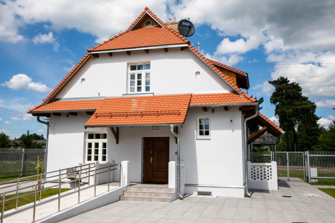 Dwukondygnacyjny dom ze spadzistym czerwonych dachem, podjazd dla wózków. 