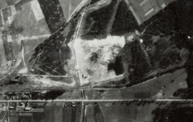 Zdjęcie lotnicze, teren poobozowy w kształcie przypominającym kwadrat o jasnym kolorze, dookoła pasma zieleni. 