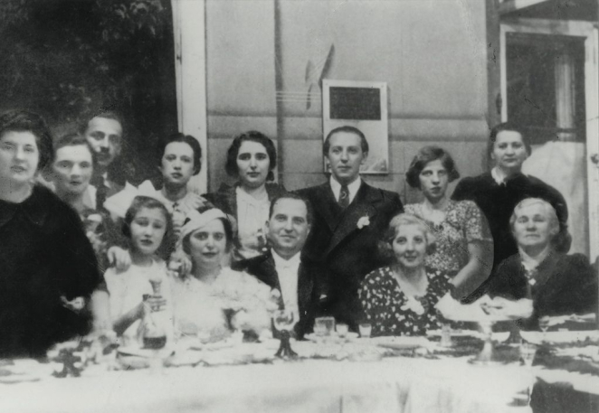 Portret wielopokoleniowej rodziny, w pierwszym rzędzie mężczyzna i kobieta w średnim wieku, kobieta ubrana na biało. 