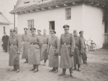 Grupa mężczyzna w niemieckich mundurach na tle białego domu. 