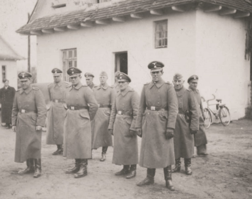 Grupa mężczyzna w niemieckich mundurach na tle białego domu. 