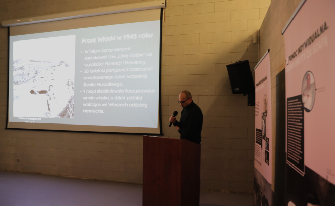 Prelegent przemawia przy mównicy podczas seminarium, na tle slajdu prezentacji