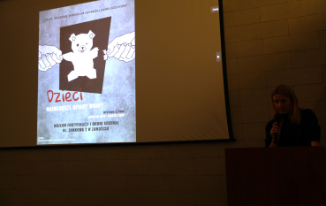 Prelegentka przemawia podczas seminarium, a na ekranie wyświetlony jest slajd prezentacji z rozrywanym pluszowym misiem i napisem: Dzieci najmłodsze ofiary wojny.