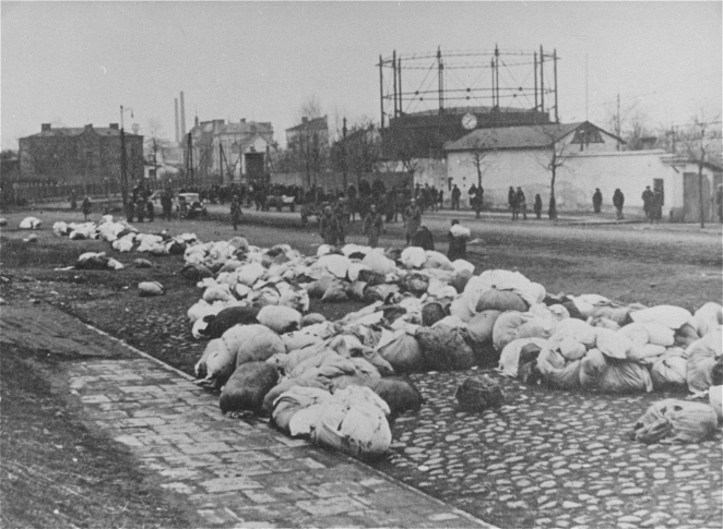 Fotografia przedstawiająca rampę kolejową w Drohobyczu, na której znajdują się liczne tobołki i bagaże. W tle widoczni są ludzie i zabudowania miejskie.