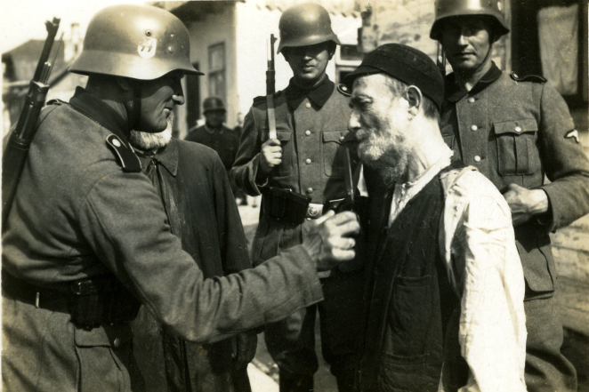 Niemieccy żołnierze otaczają starszego żydowskiego mężczyznę. Jeden z żołnierzy obcina mu brodę.