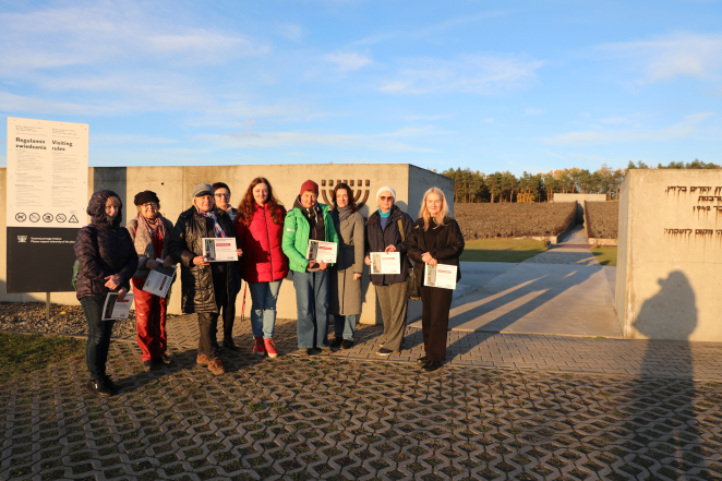 Grupa kobiet stoi przed pomnikiem w Miejscu Pamięci w Bełżcu, trzymając w dłoniach certyfikaty uczestnictwa w seminarium.