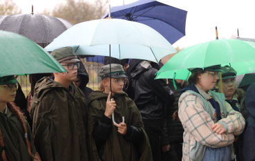 Grupa harcerzy stoi pod parasolami.