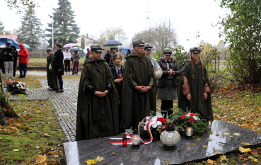Grupa młodzieży szkolnej w harcerskich mundurach i pelerynach przeciwdeszczowych oddaje hołd ofiarom.