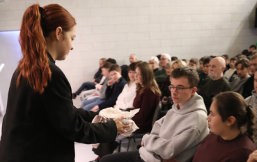 Młoda ruda kobieta rozdaje macę publiczności.