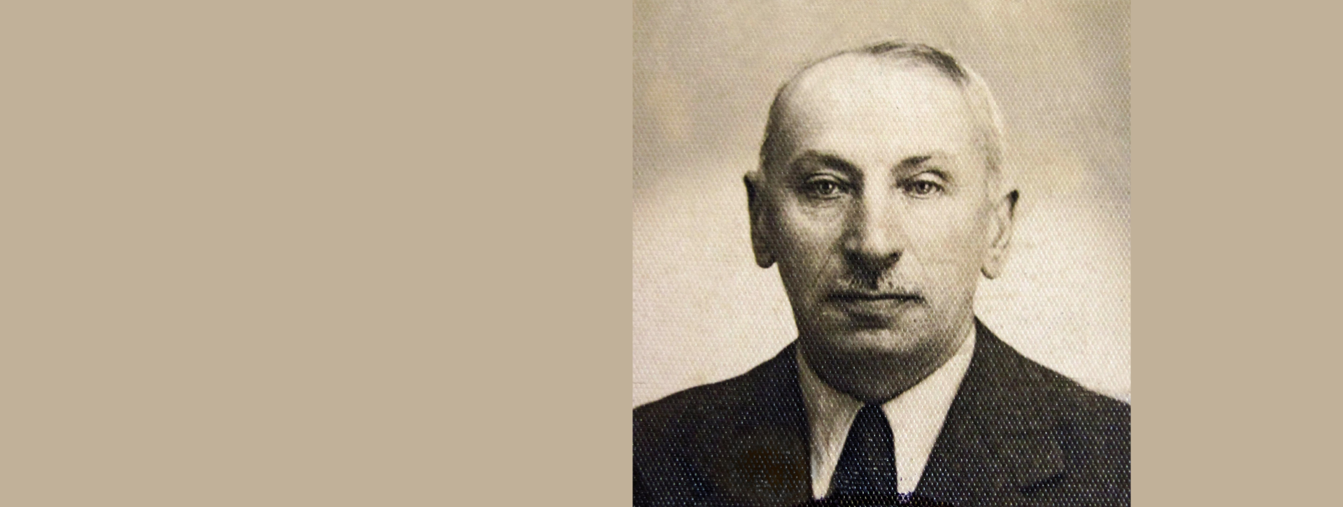 Czarno-białe, archiwalne zdjęcie portretowe mężczyzny w garniturze i krawacie. Postać ma wąsy i wysokie czoło. Na dole zdjęcia widnieje fragment pieczątki urzędowej. 