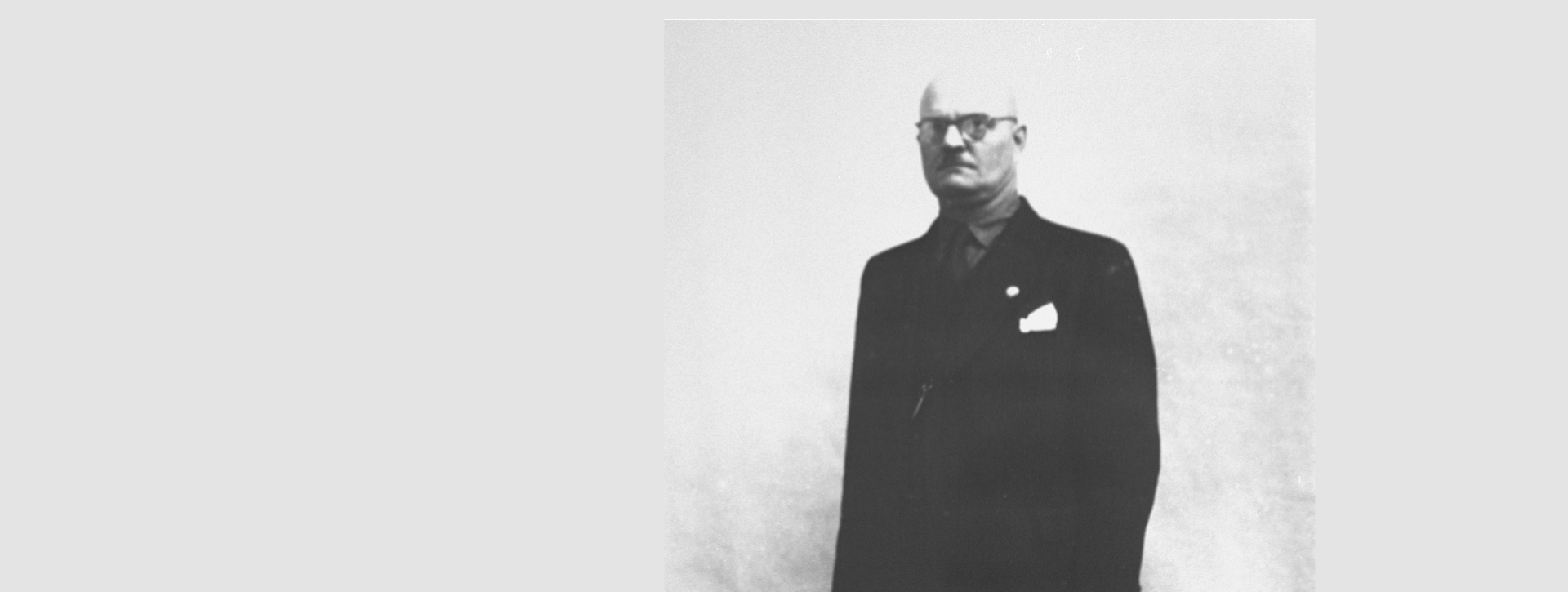 Czarno-biała, archiwalna fotografia przedstawiająca dorosłego mężczyznę, który stoi przodem do widza, lekko zwrócony w lewą stronę z wyprostowaną sylwetką i rękami opuszczonymi wzdłuż ciała.