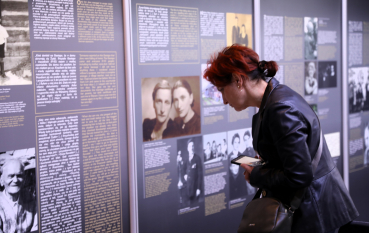 Kobieta pochyla się nad panelem wystawowym, uważnie czytając umieszczone na nim teksty w dwóch językach.
