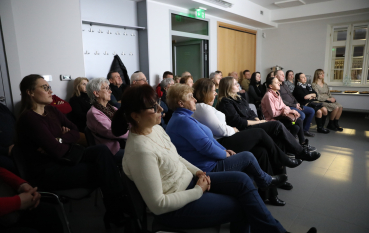 Widzowie siedzący w rzędach, skupieni na oglądaniu projekcji w ciemnym pomieszczeniu.