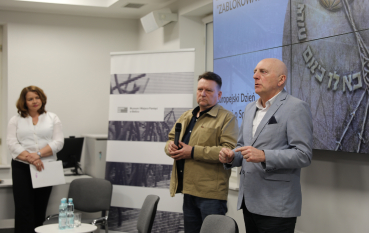 Zbliżenie na dwóch prelegentów podczas rozmowy; mężczyzna w niebieskiej marynarce wyjaśnia kwestię, gestykulując dłońmi.