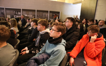 Grupa uczniów siedzi w rzędach, z uwagą słuchając wykładu w sali edukacyjnej.