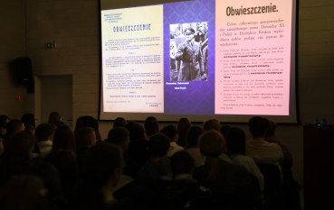 kran projekcyjny wyświetlający historyczne obwieszczenia oraz zdjęcie mężczyzny w mundurze przed zaciemnioną widownią.