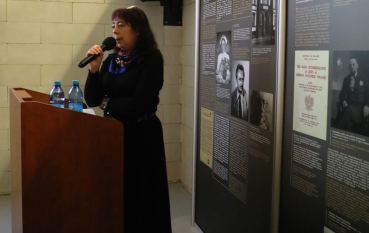 Kobieta przy mównicy obok paneli edukacyjnych.