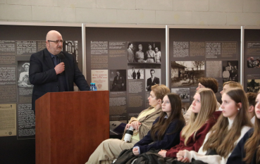 Prelegent przy mównicy omawia treści prezentowane na panelach ściennych przed młodzieżą.