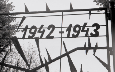 A black-and-white photograph. A close-up of a metal gate with the dates ‘1942–1943’ welded onto it.