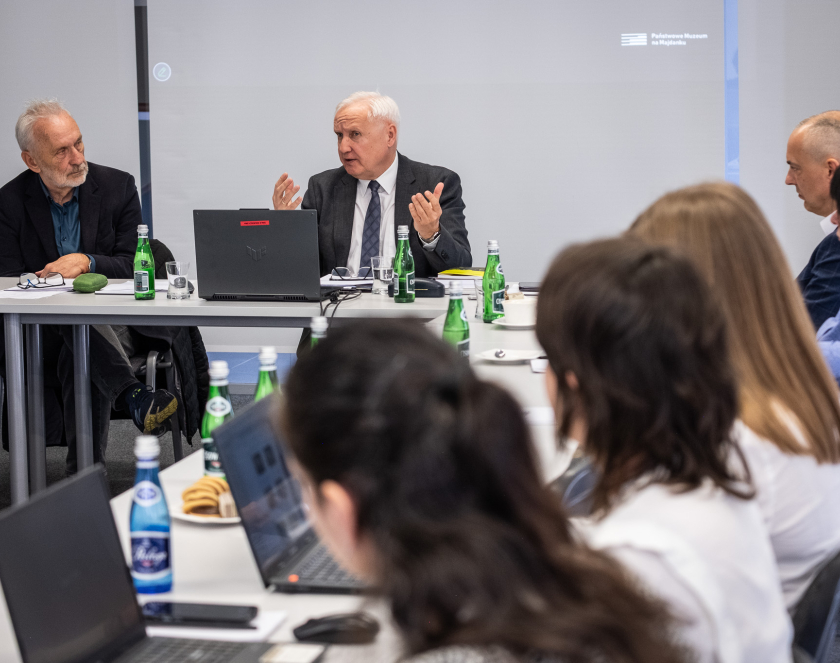 Grupa osób ubranych elegancko siedzących przy stołach. 