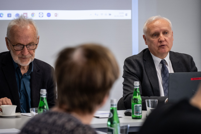 Dwóch starszych mężczyzn przy stole, w tle prezentacja. 