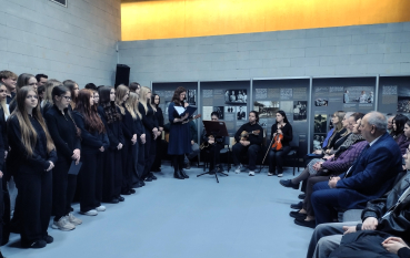 Szerokie ujęcie sali w Muzeum i Miejscu Pamięci w Bełżcu. Po lewej grupa młodzieży, w głębi zespół muzyczny, a po prawej siedzący goście. Na ścianach ekspozycja historyczna.