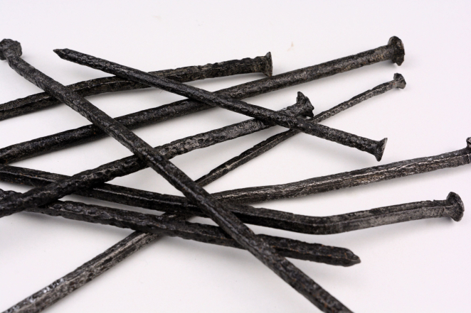 Czarne długie gwoździe na białym tle odkryte podczas badań archeologicznych na terenie poobozowym.
