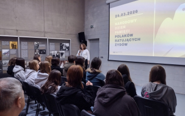 Prelegentka w białej bluzce przemawia do grupy młodzieży w sali muzealnej. Na ekranie widnieje napis: „24.03.2026 Narodowy Dzień Pamięci Polaków ratujących Żydów”.