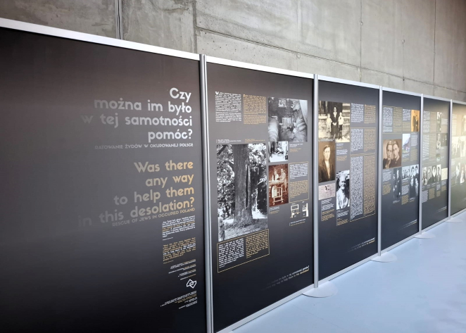 Rząd ciemnych paneli wystawowych ustawionych w nowoczesnym wnętrzu o surowych, betonowych ścianach. Pierwszy plan zajmuje tablica z dużym napisem w języku polskim i angielskim: „Czy można im było w tej samotności pomóc? Ratowanie Żydów w okupowanej Polsce”. Na kolejnych planszach widoczne są archiwalne fotografie, biogramy oraz opisy historyczne