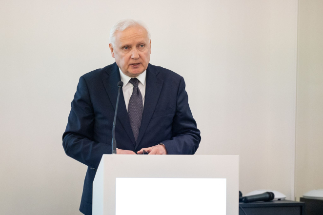 Starszy mężczyzna w garniturze przemawia do mikrofonu.