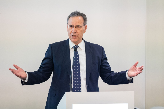 Starszy mężczyzna w garniturze, rozkłada ręce i przemawia do mikrofonu.