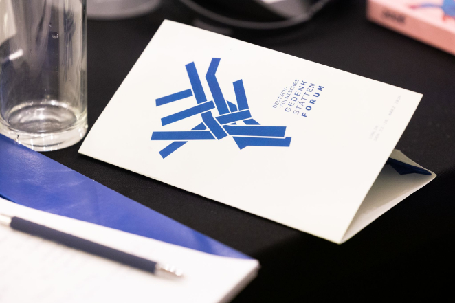 Drukowany program, niebieskie logo przedstawiające geometryczne drzewo, poniżej napis FORUM, po lewej szklanka.