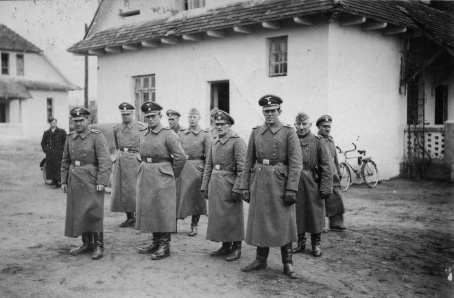 Czarno-białe zdjęcie. Brukowany chodnik, po jego stronach rosnące w góry ściany, żeliwne druty. W tle drzewa