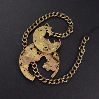 The photograph shows two heavily damaged brass components of a watch mechanism accompanied by a thick-linked chain