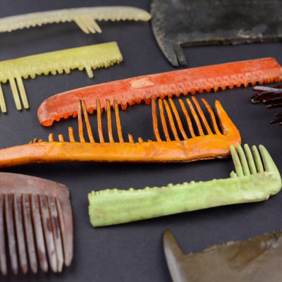 Close-up of several broken and incomplete combs laid out on a dark background. The items are in various colors: orange, green, yellow, brown, and black. Many have missing teeth and show signs of having been buried in the ground for many years